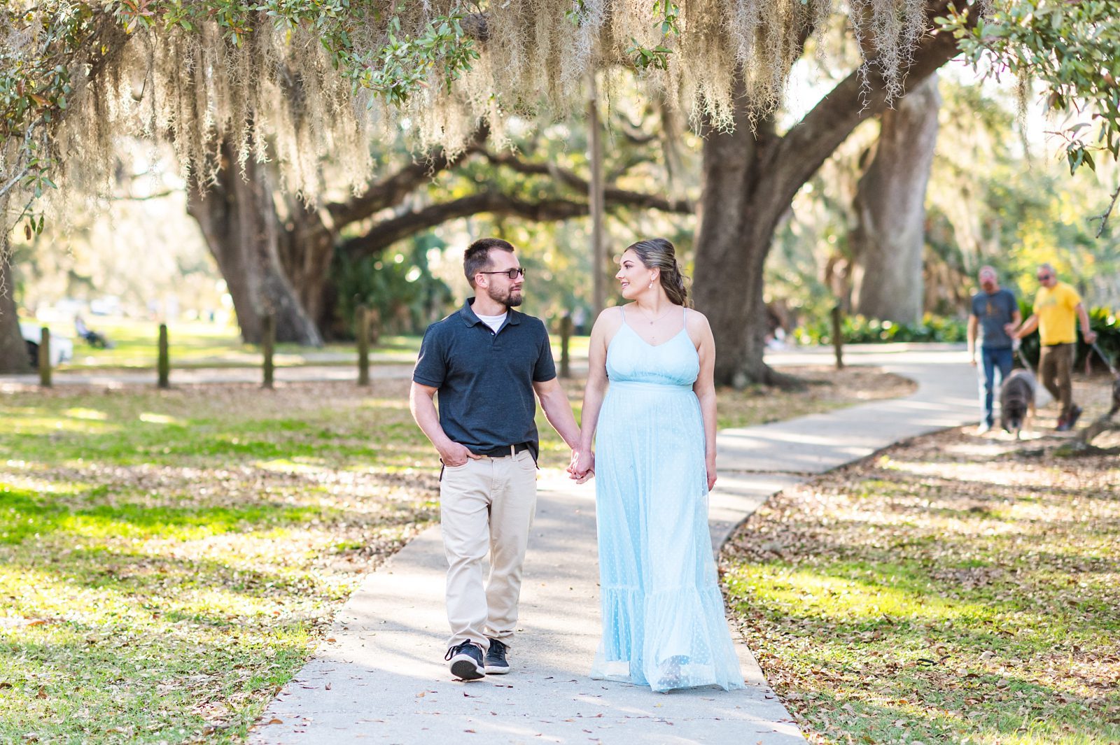 Salena and Trey walking under oak trees during their City Park engagement session in New Orleans