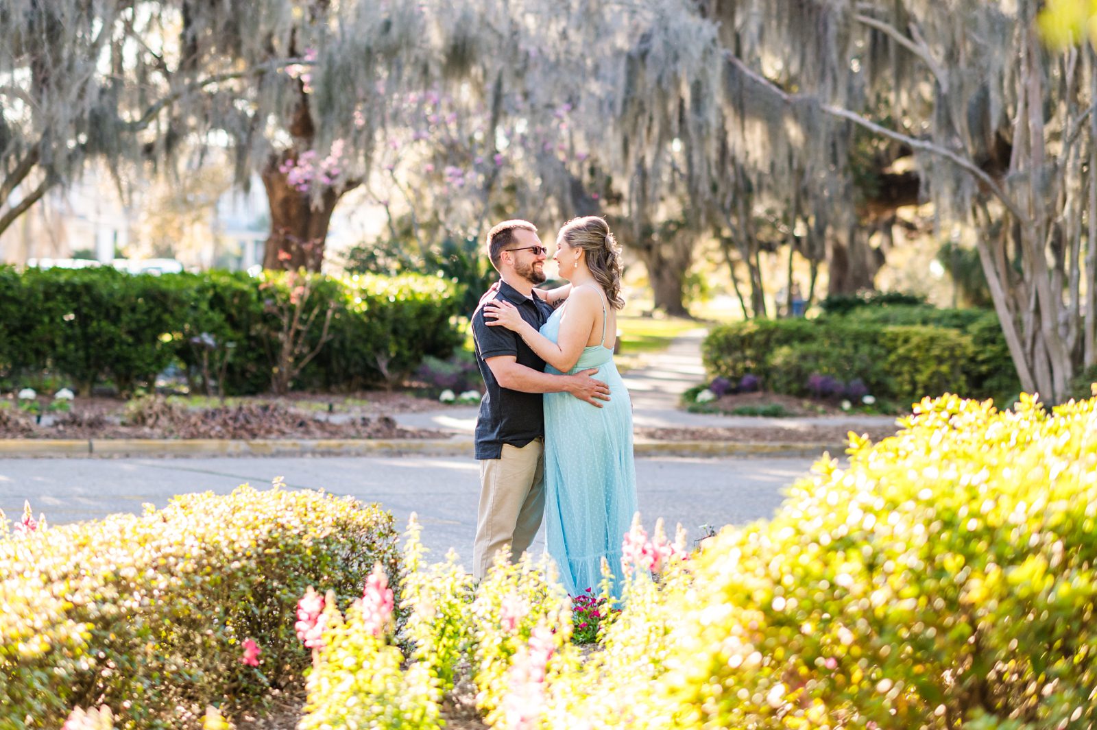 Couple embracing near a pathway lined with oak trees at City Park.