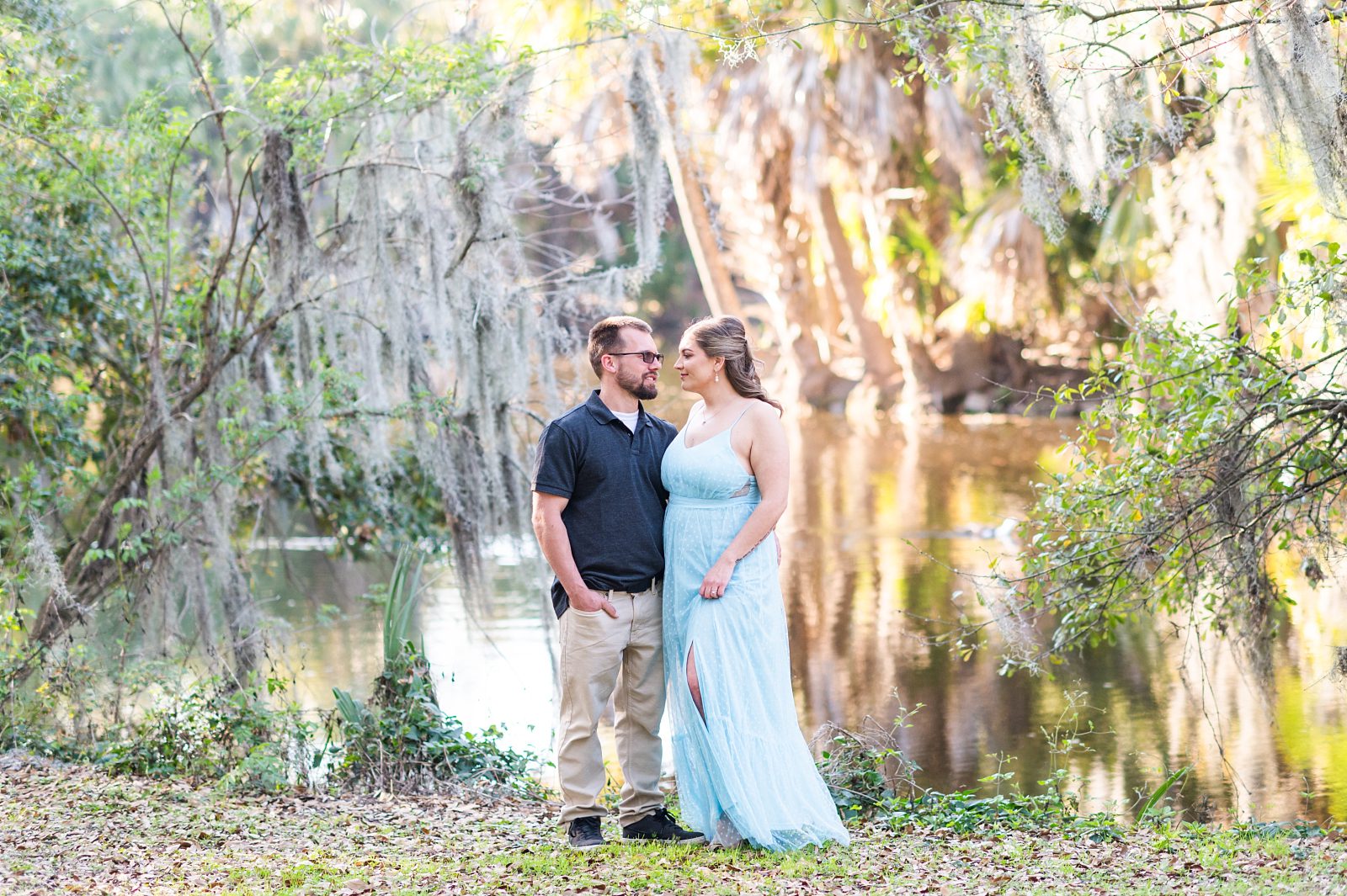 Engaged couple smiling at each other in front of the lagoon at City Park
